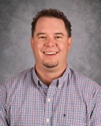 Smiling man in a checkered shirt against a gray studio backdrop