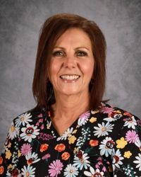 Smiling woman in a black floral blouse against a gray studio backdrop