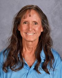 A woman with long brown hair is wearing a lighter blue shirt and smiling for the camera.