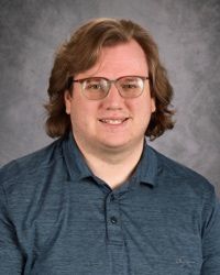 Portrait of a person wearing glasses and a blue polo shirt against a gray backdrop