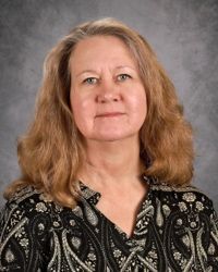 Portrait of a woman with long blonde hair, wearing a black patterned top against a gray studio backdrop