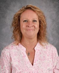 Smiling woman in a pink patterned blouse against a gray studio backdrop