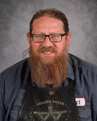 Portrait of a smiling man with glasses and a long beard against a gray backdrop
