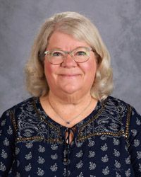A woman wearing glasses and a dark blue shirt with light blue print is smiling for the camera.