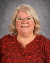 Smiling person in glasses and a red patterned top against a gray studio backdrop