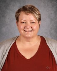 Studio portrait of a smiling person in a red top and gray cardigan against a gray backdrop