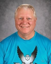 Smiling man in a bright blue T-shirt with an eagle graphic against a gray studio backdrop