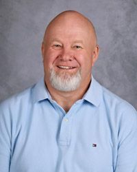 A bald man with a beard is wearing a blue shirt and smiling for the camera.