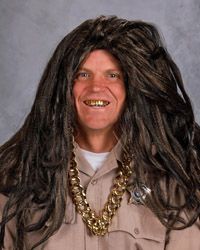 A man wearing a long wig and gold chain around his neck looking at the camera.