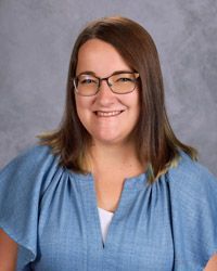 A woman wearing glasses in a blue and white shirt is smiling for a picture.
