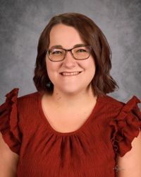 A woman wearing glasses in a blue and white shirt is smiling for a picture.