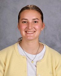 A young woman hair pulled back wearing a yellow sweater and white shirt is smiling for the camera.