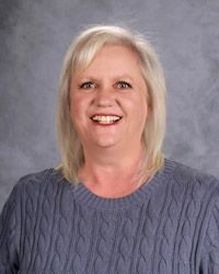 Woman with blonde hair wearing a blue sweater, smiling, in front of a gray backdrop.