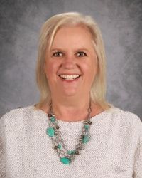 Smiling woman in a white sweater and turquoise necklace against a gray studio backdrop