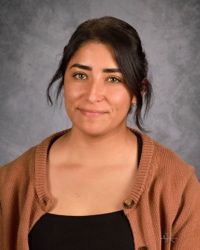 Portrait of a woman with dark hair, wearing a brown cardigan against a gray studio backdrop