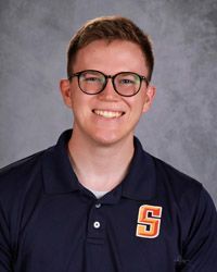 A young man with glasses wearing a black polo shirt with Snow College is smiling for the camera.