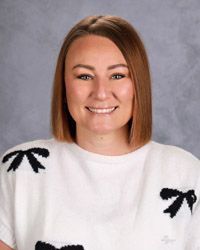 A woman with short mid length brown hair in a white shirt with black bows is smiling for the camera.