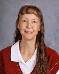 A woman in a rwhite shirt and red sweater is smiling for a picture.