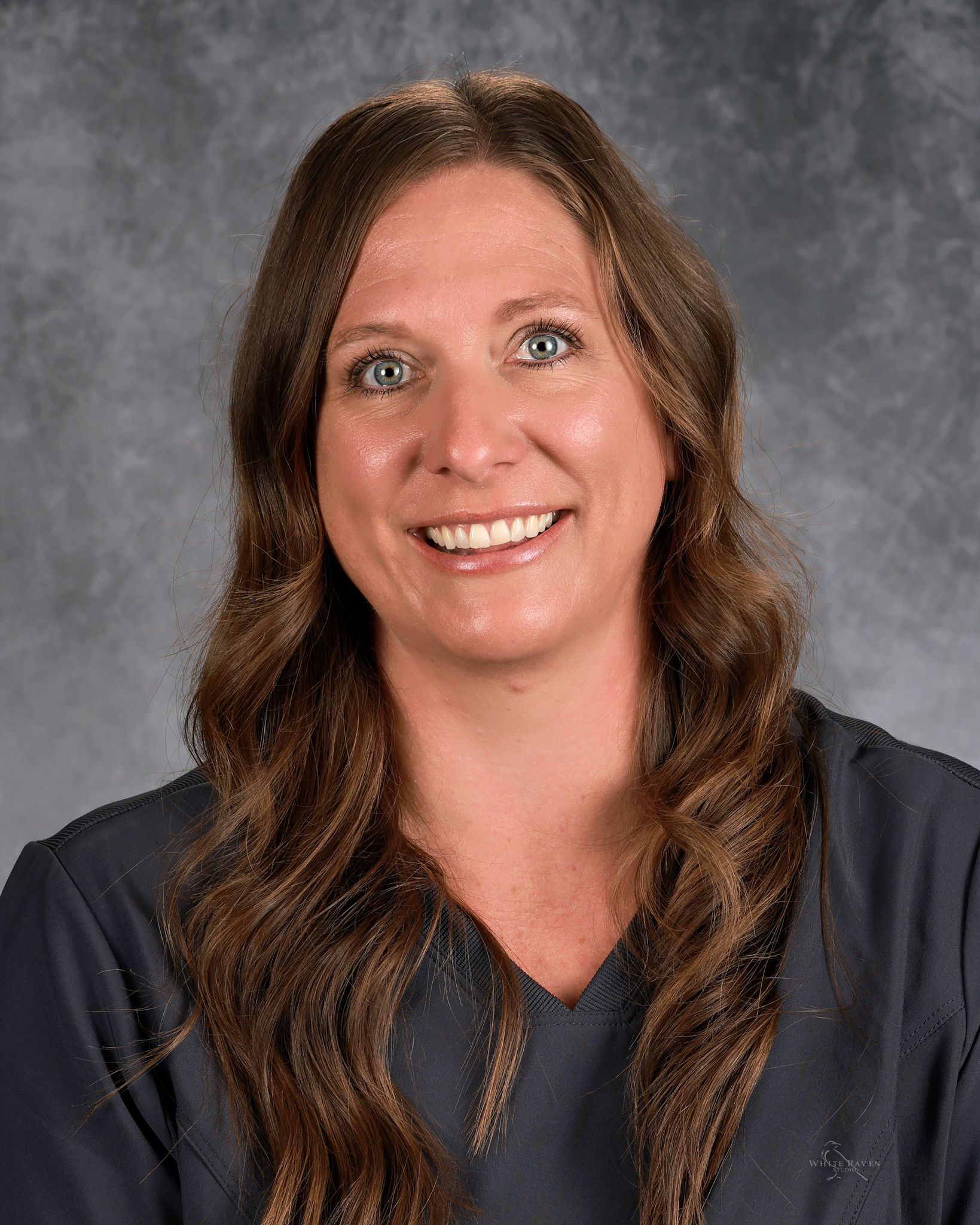 A woman in dark gray scrub top is smiling for the camera.