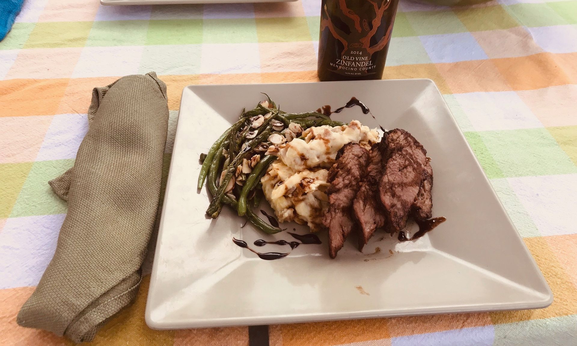 A white plate topped with meat and green beans on a table.
