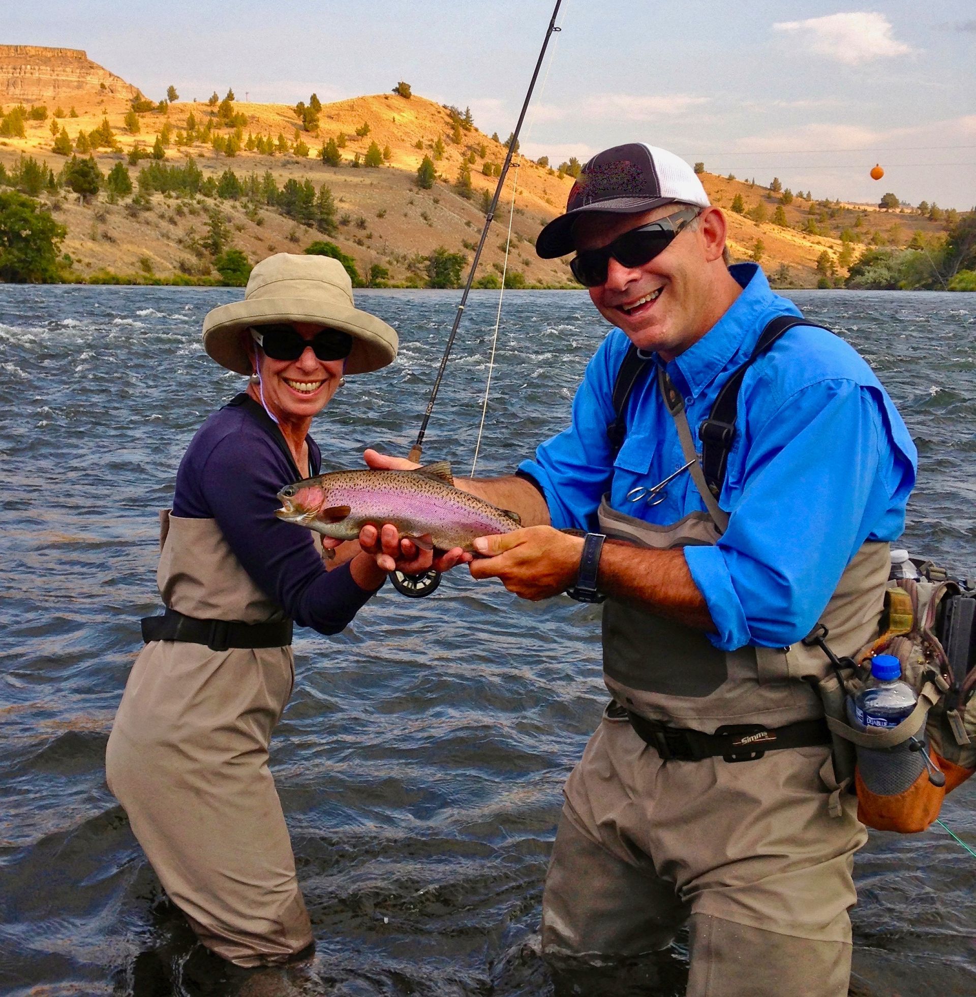A man and a woman holding a rainbow trout in the water
