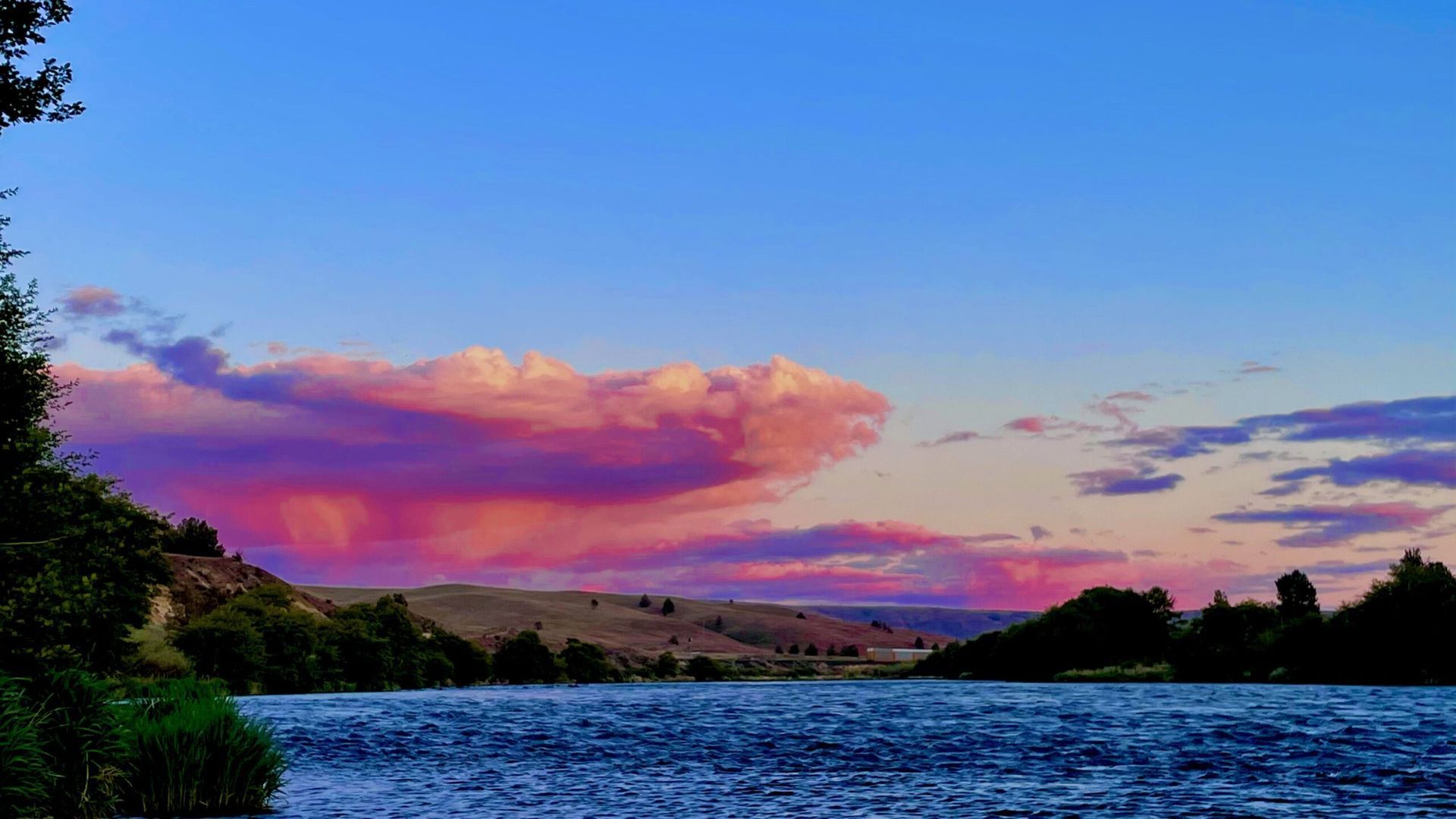 A lake with a sunset in the background and pink clouds in the sky.