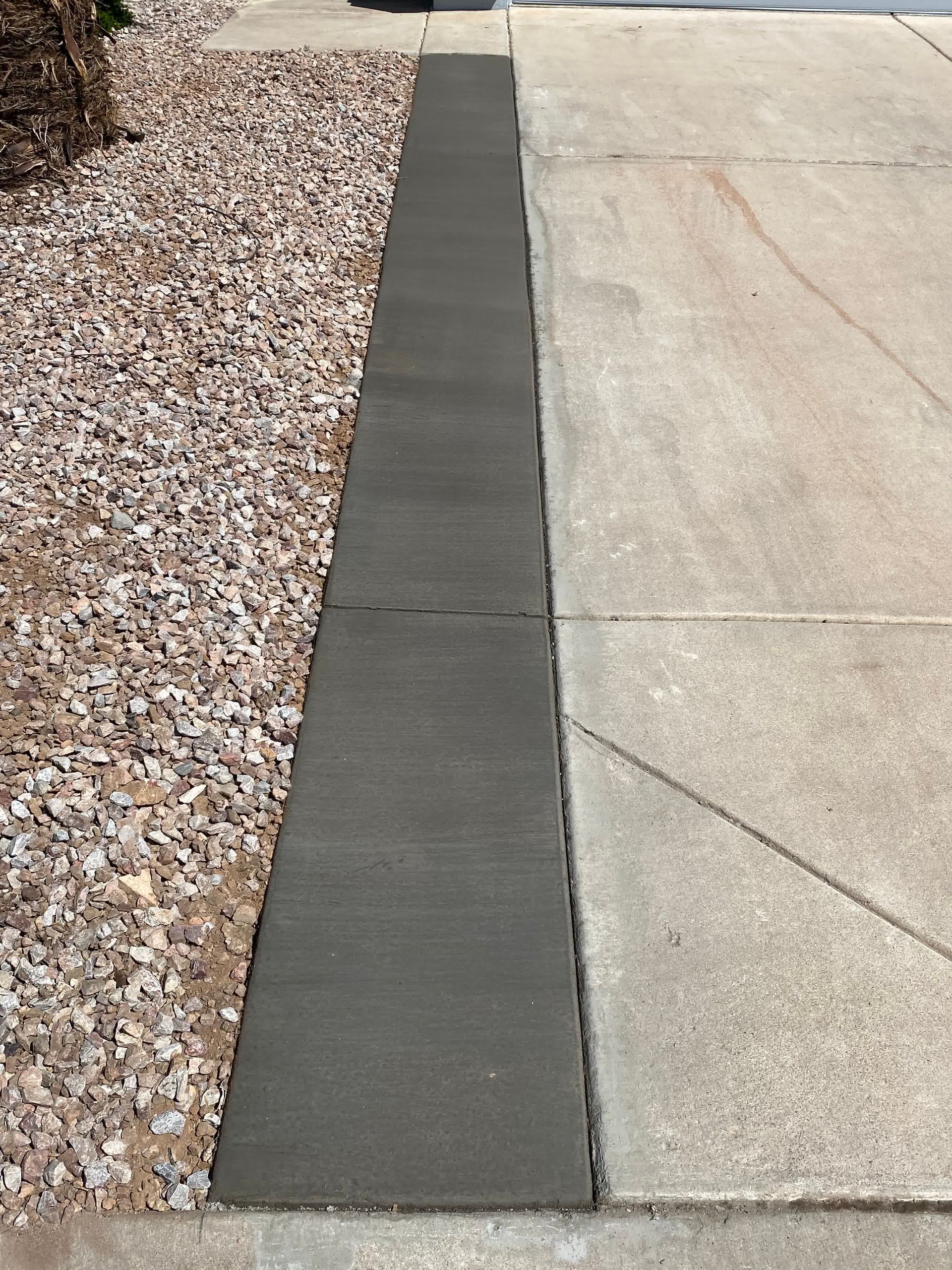 A sidewalk with a concrete curb and gravel in the background.