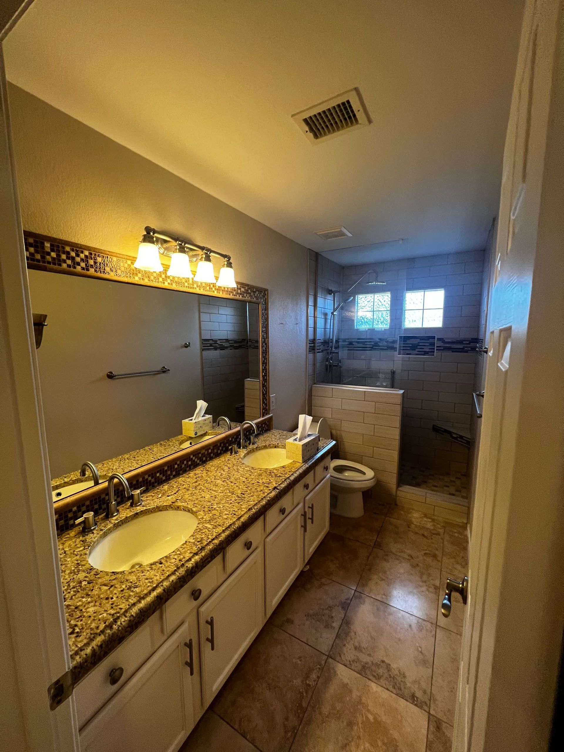 A bathroom with two sinks , a toilet , and a large mirror.