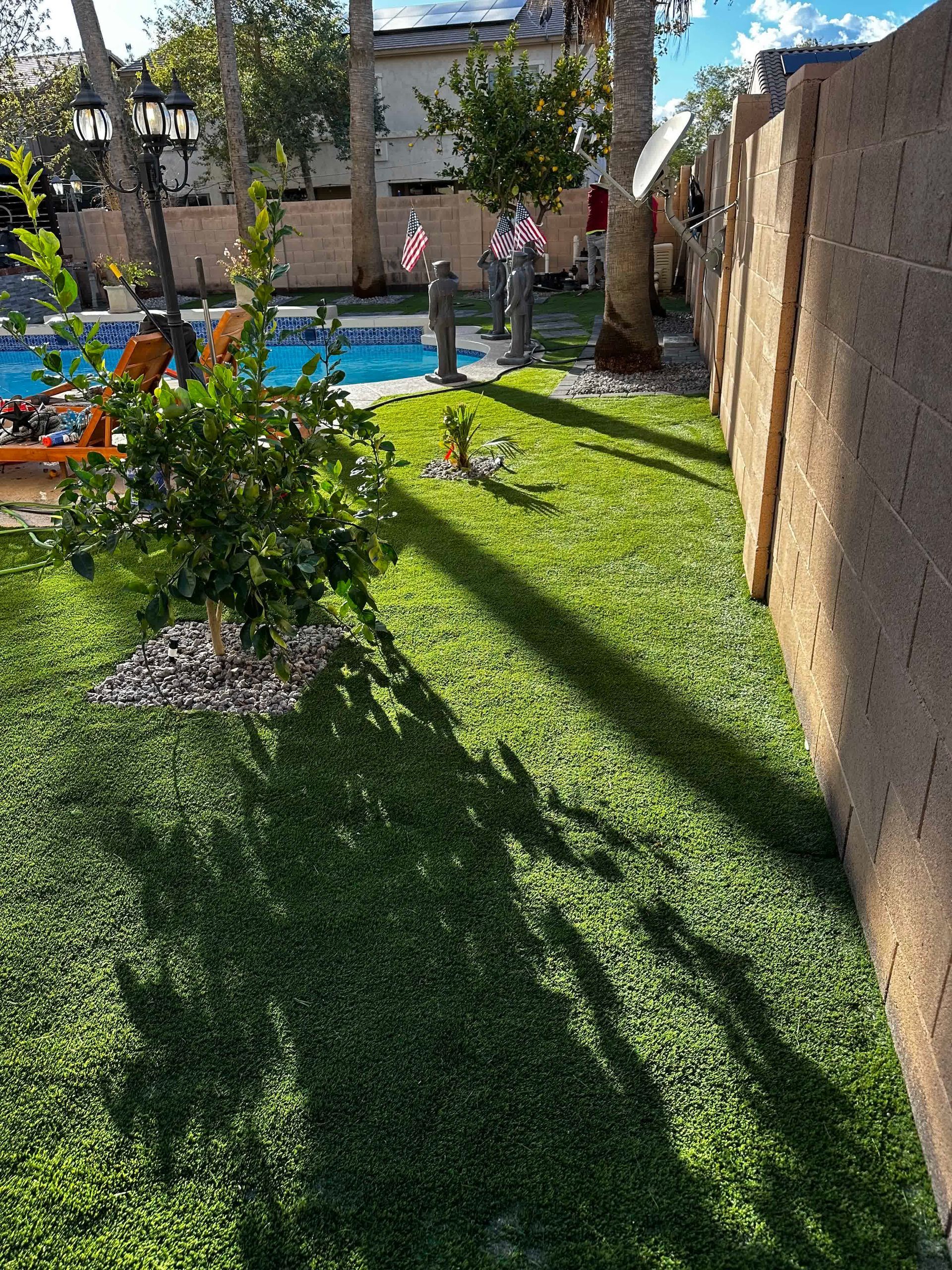 A lush green lawn with a fence and a pool in the background.