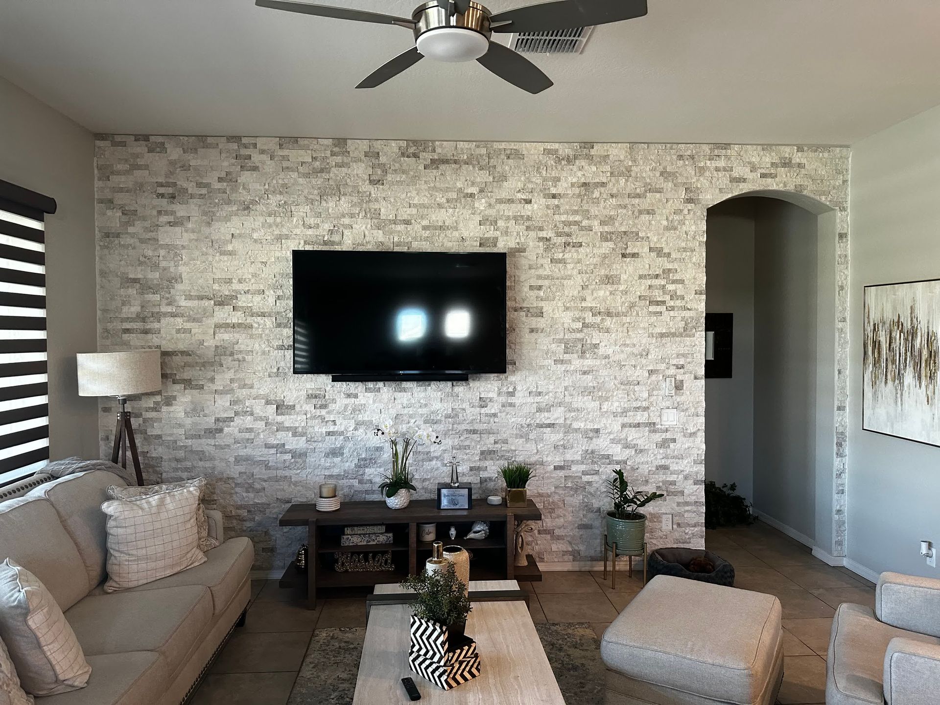 A living room with a ceiling fan and a flat screen tv on the wall.