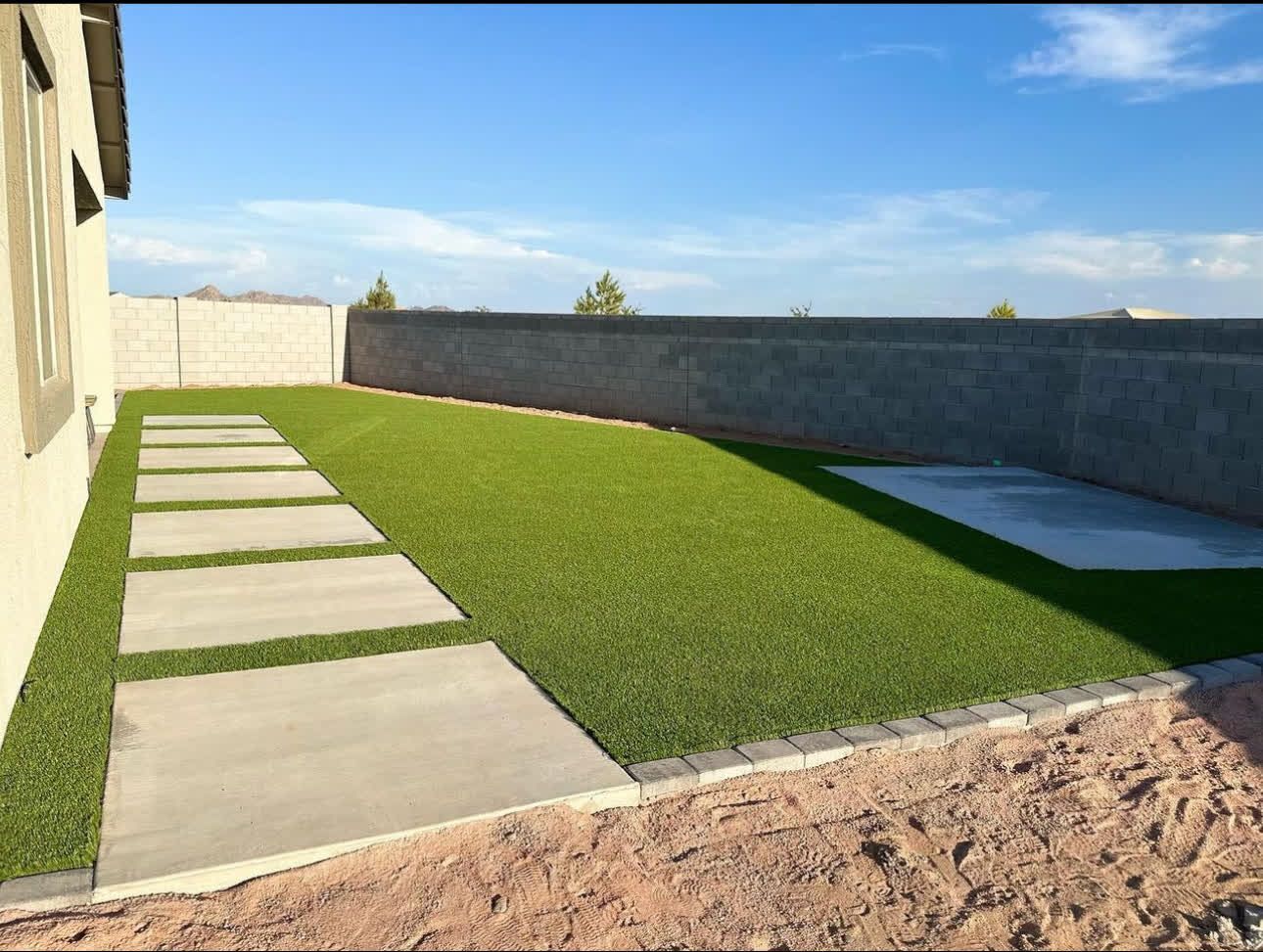 A backyard with a concrete walkway and a lush green lawn.