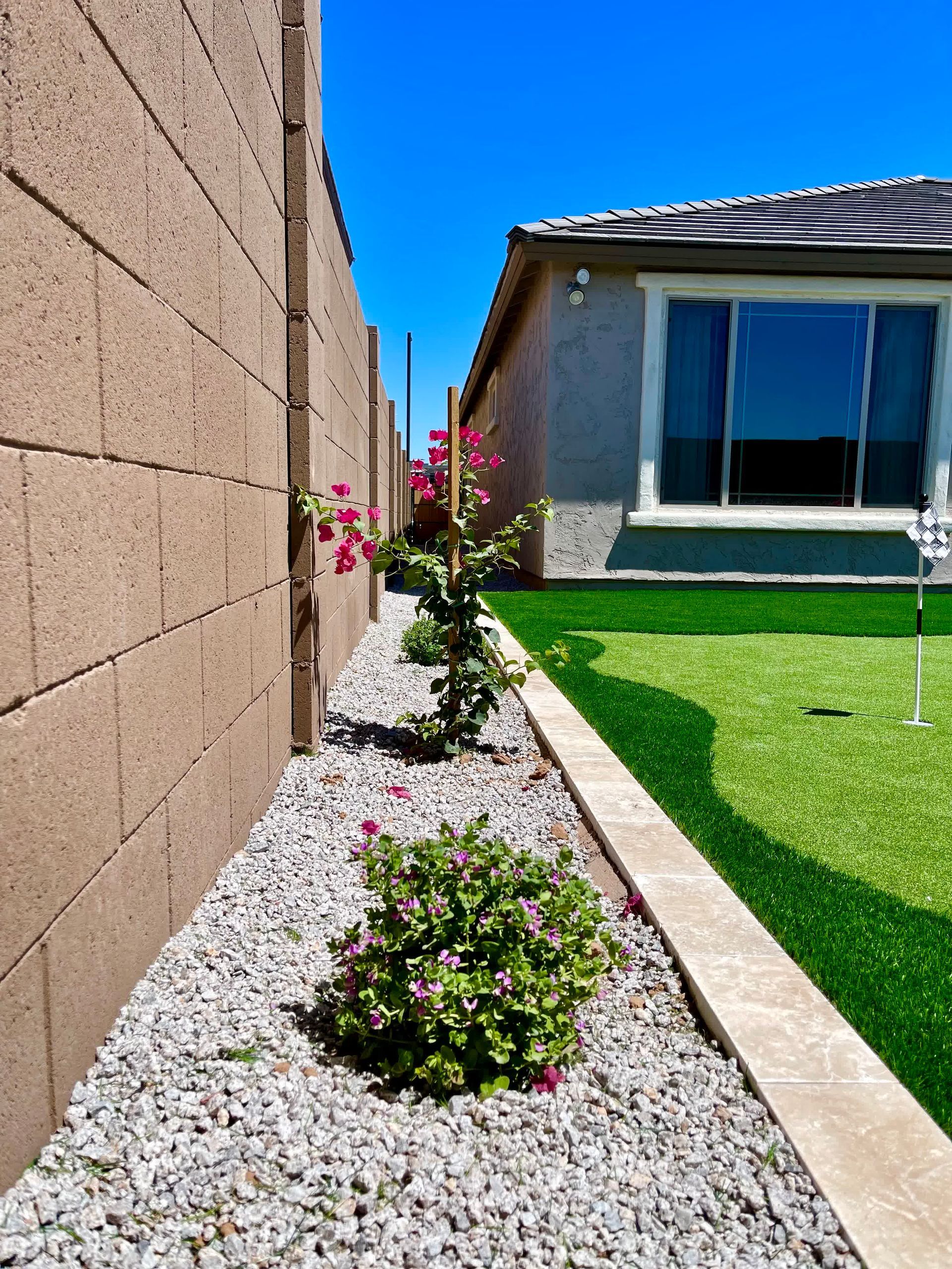 A house with a brick wall and a gravel garden in front of it.