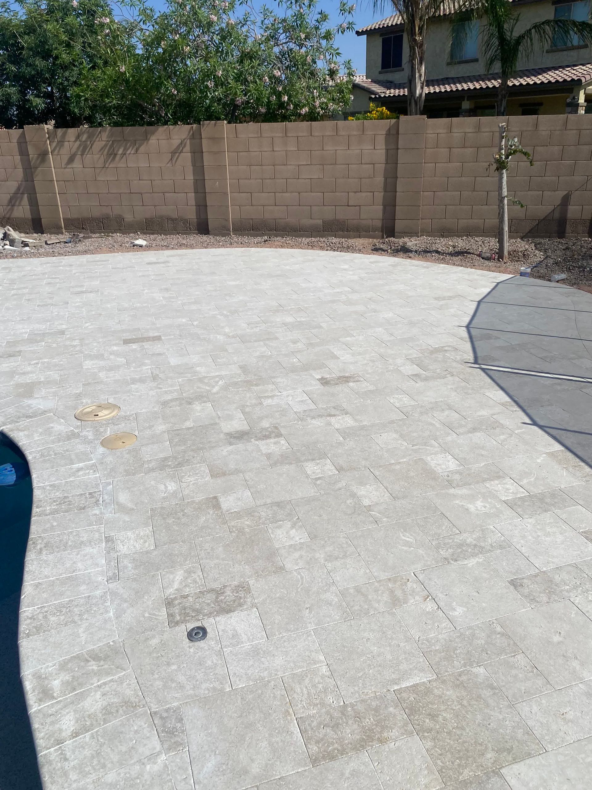 A brick wall is behind a concrete driveway in a backyard.