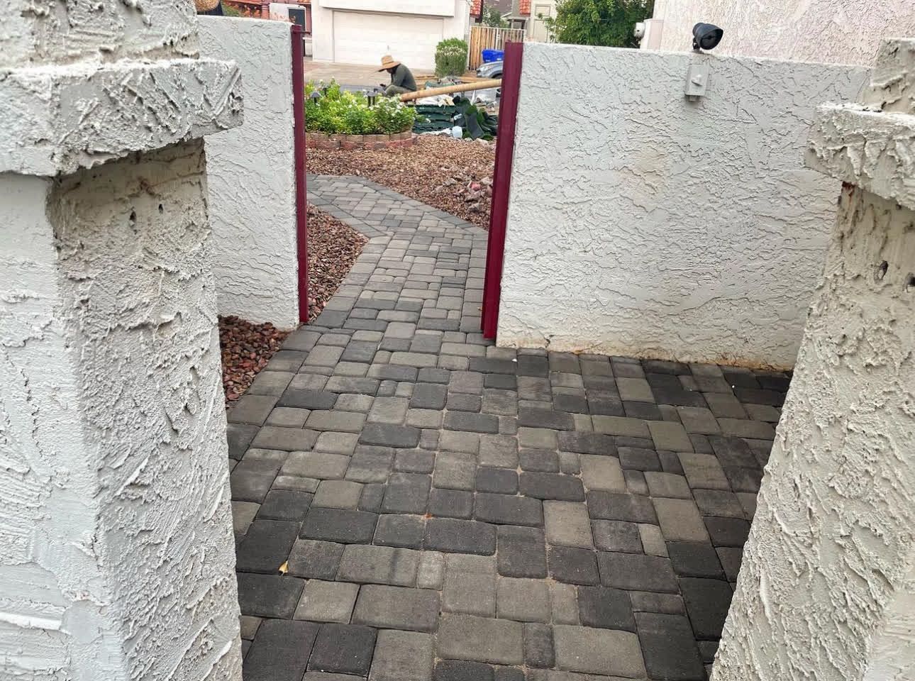 A brick walkway between two white walls with a red gate