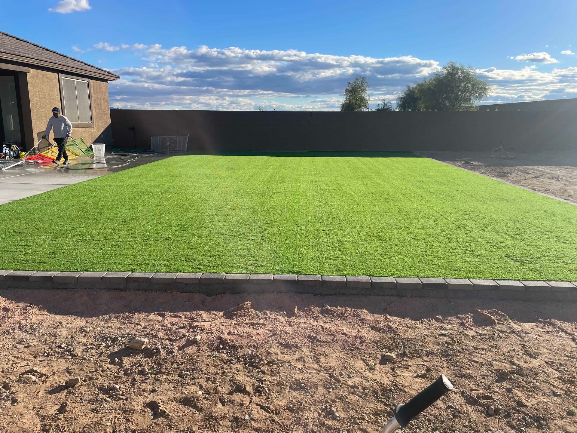 A large lawn with a sprinkler in the middle of it in front of a house.