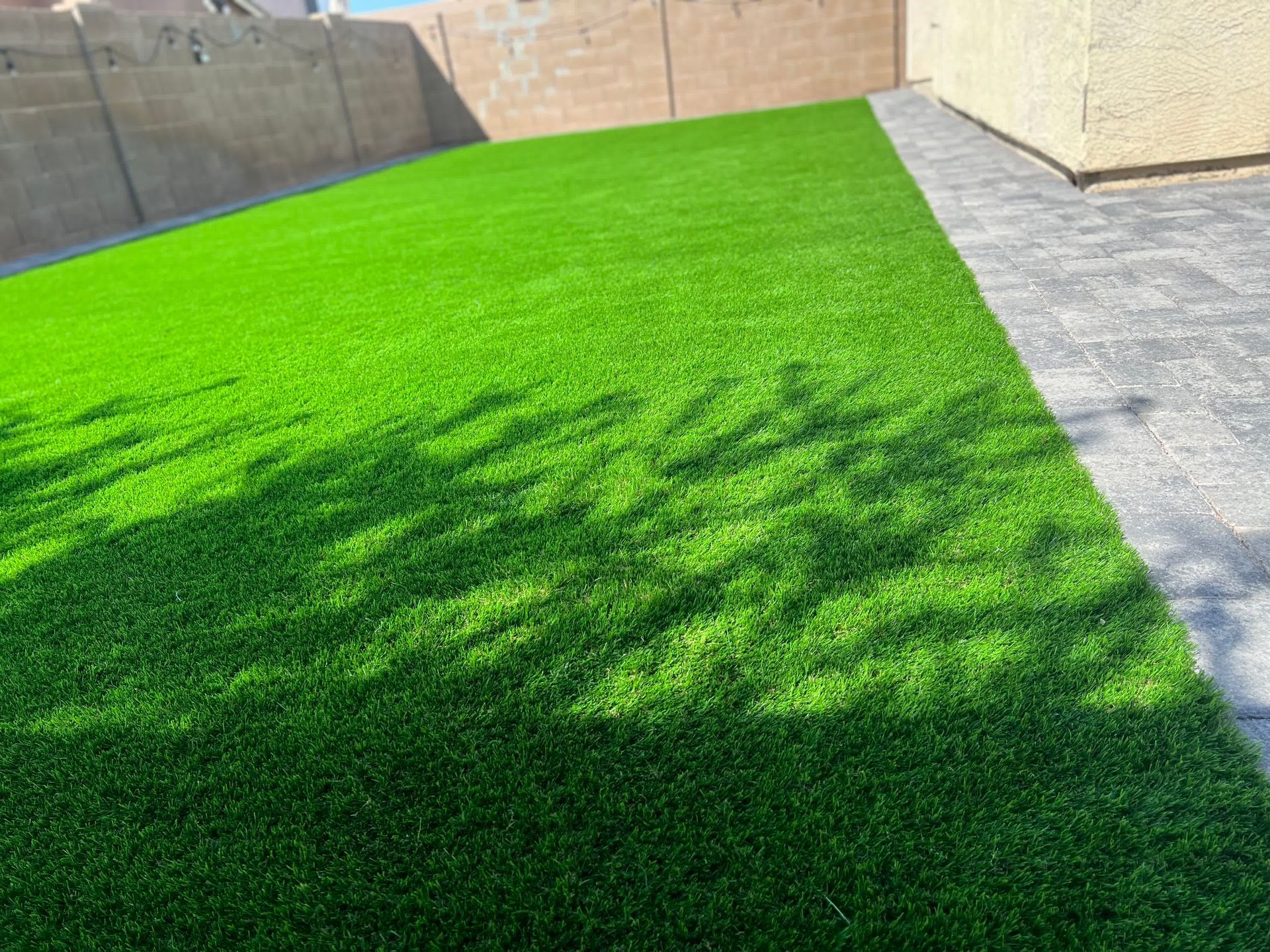 A backyard with a lot of green grass and a brick walkway.