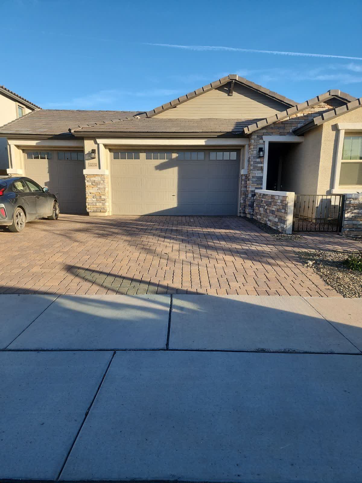 A car is parked in front of a house with two garage doors.