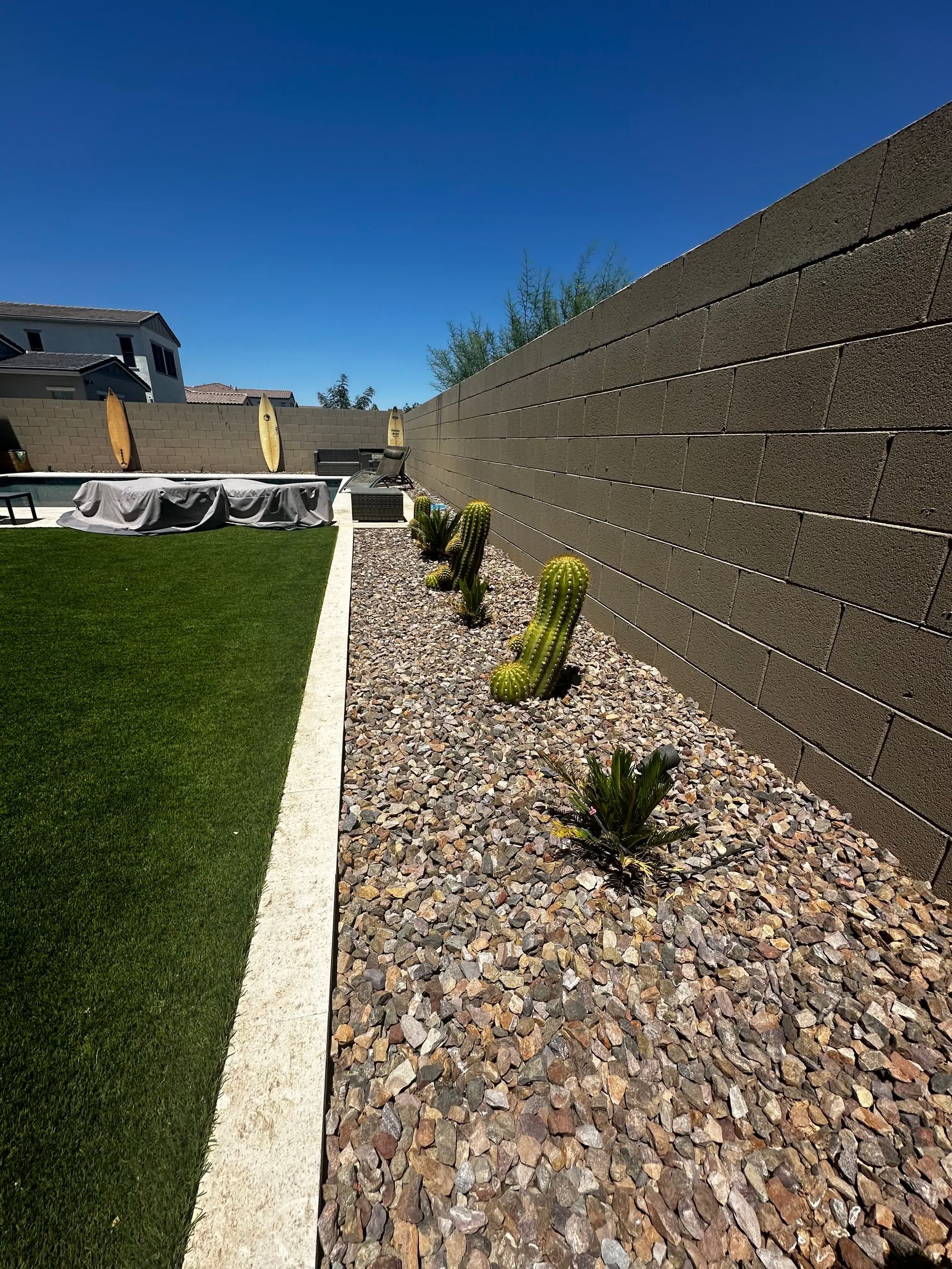 A fence surrounds a lush green backyard with rocks and plants.