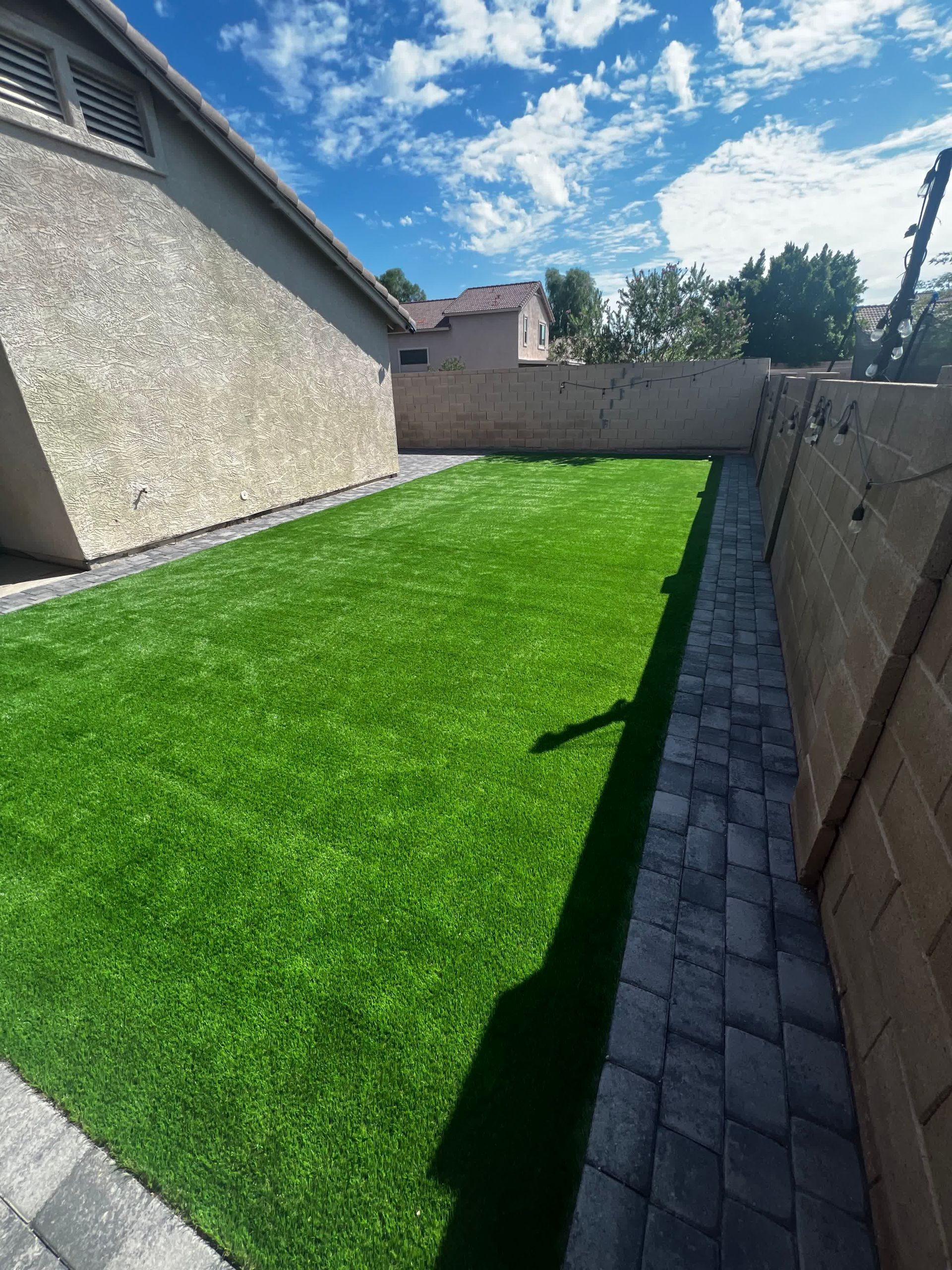 A backyard with a brick walkway and a lush green lawn.