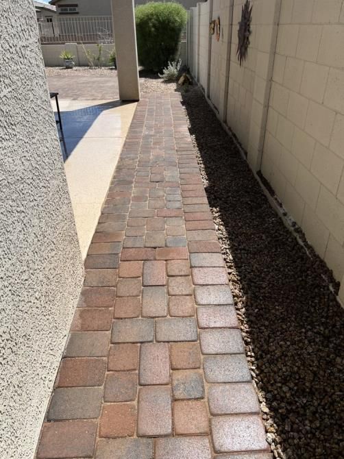 A sidewalk made of bricks is next to a brick wall.