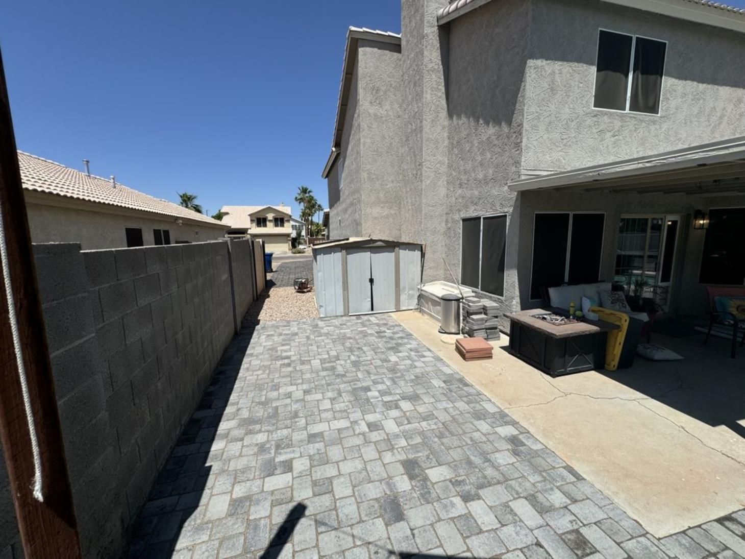 A brick walkway leading to a house with a shed in the backyard.