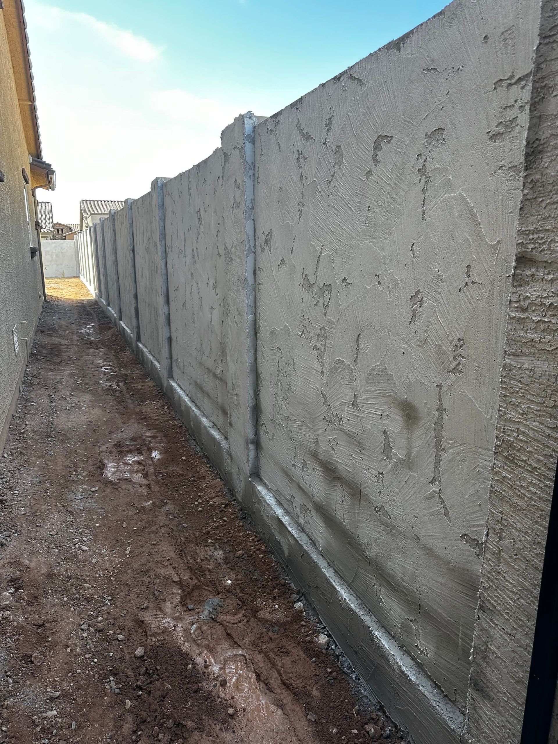 A concrete fence is being built next to a dirt road.