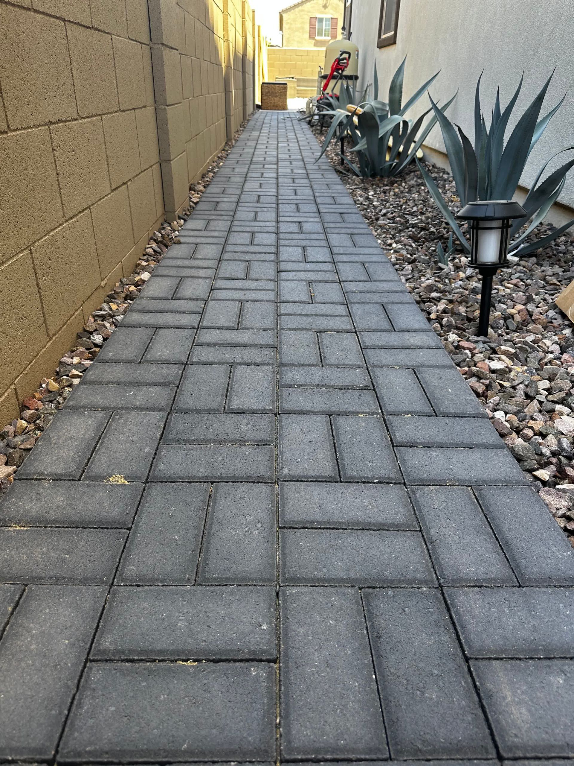 A brick walkway leading to a house next to a brick wall.