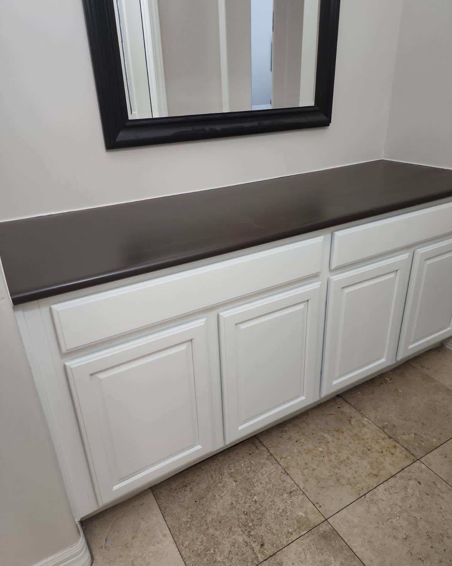 A white cabinet with a black counter top and a mirror above it.