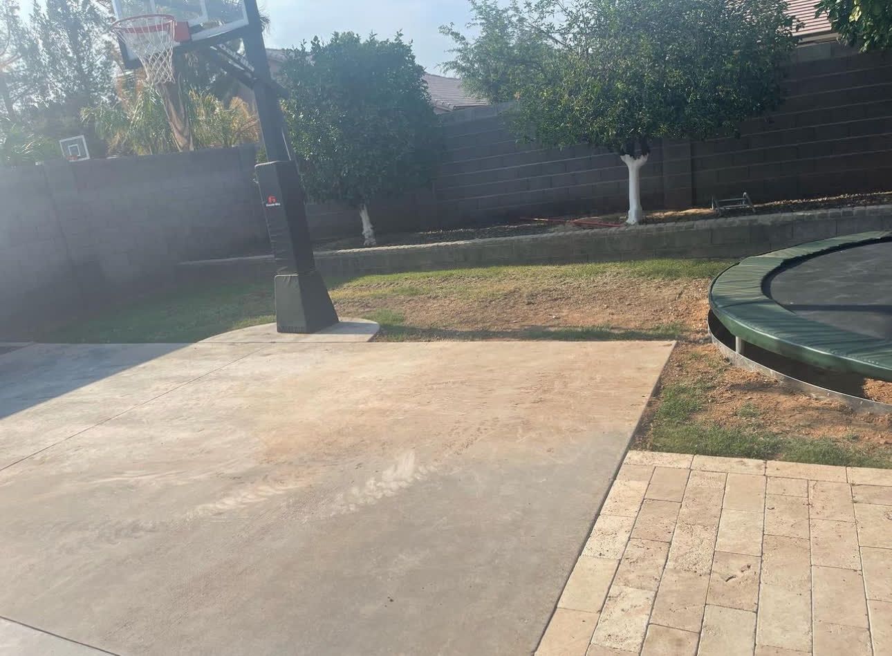 There is a trampoline in the backyard next to a basketball hoop.