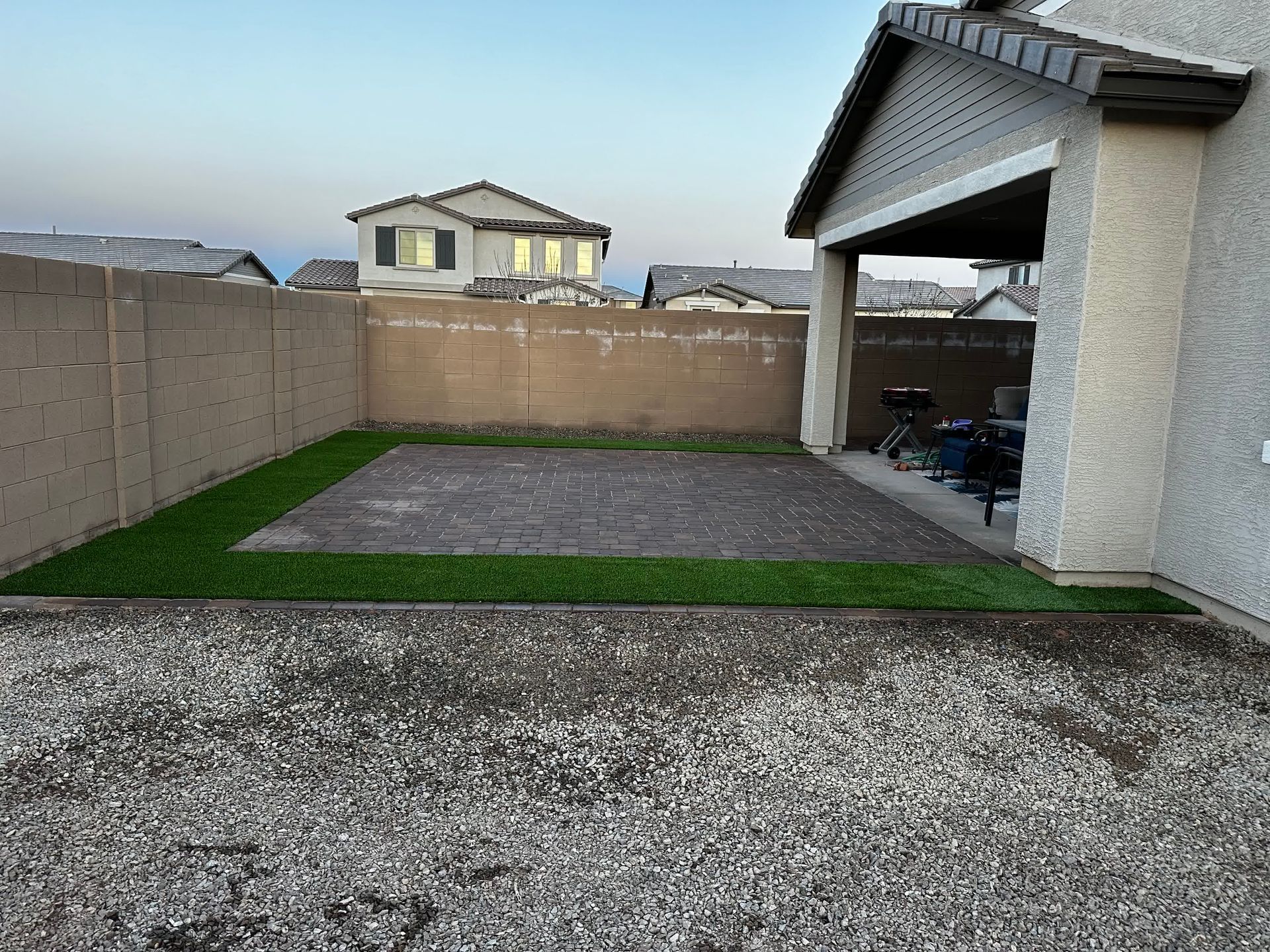 A backyard with grass and gravel in front of a house.