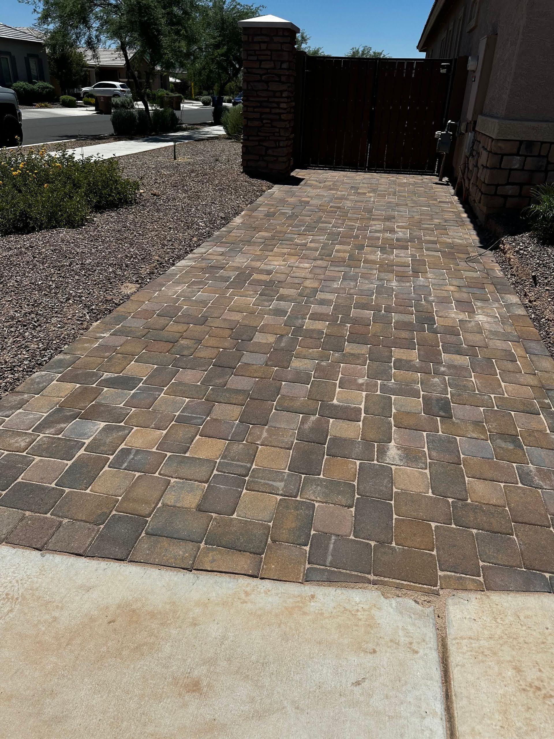 A brick walkway leading to a house with a gate in the background.