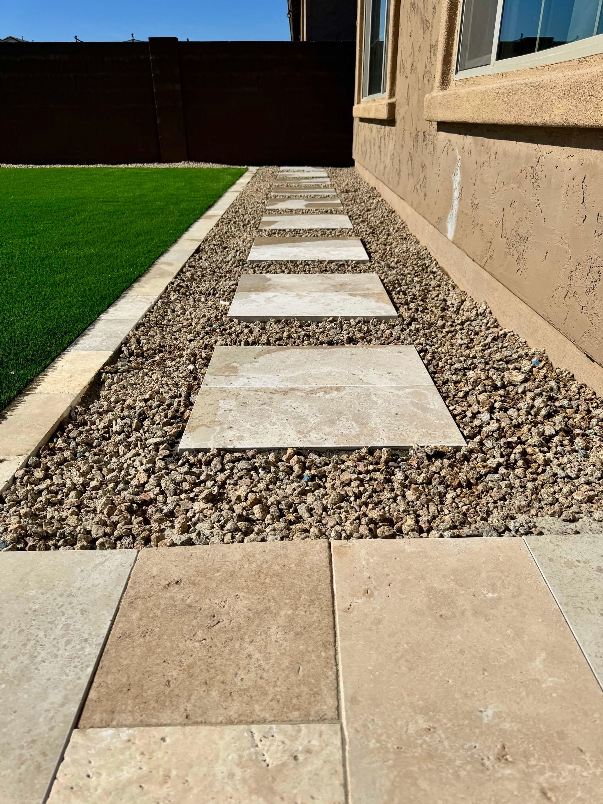 A stone walkway leading to a house with a lawn in the background