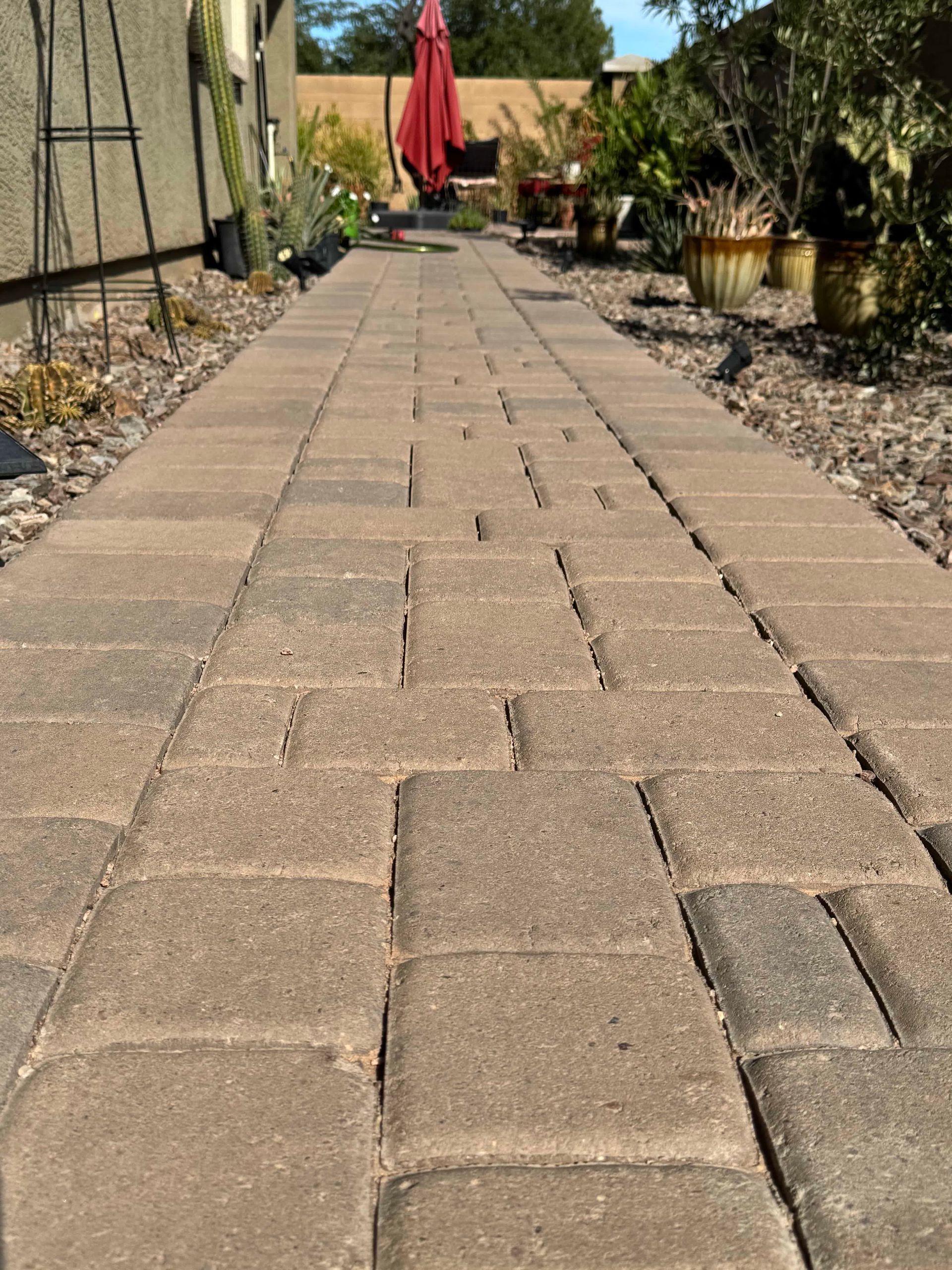 A brick walkway leading to a house with a red umbrella in the background.