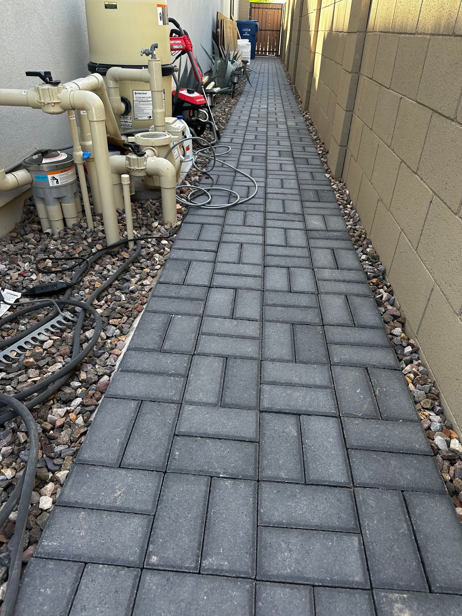 A brick walkway leading to a building with pipes on the side.